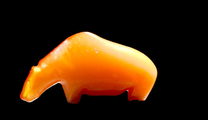 Ancient artefact resembling an animal, carved from amber, set against a black background.