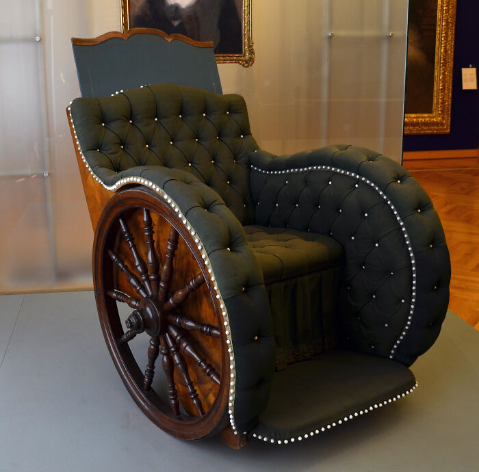 Ancient artefact: Ornate tufted chair with wooden wheels in a museum setting.