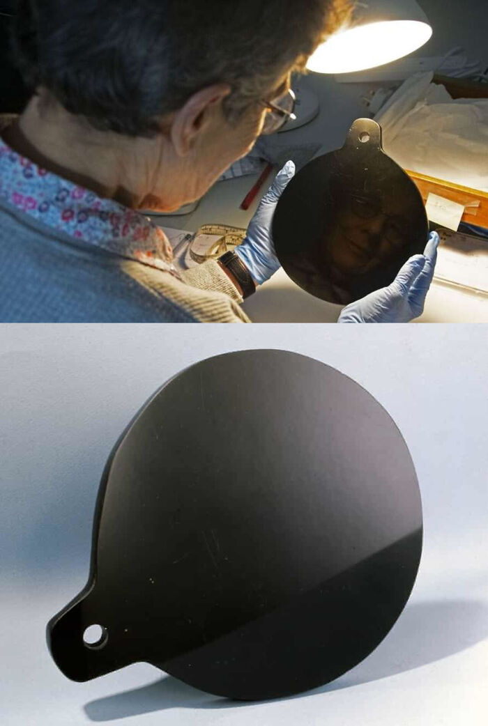 A person examines an ancient obsidian mirror under a lamp, showcasing remarkable survival of ancient artefacts.
