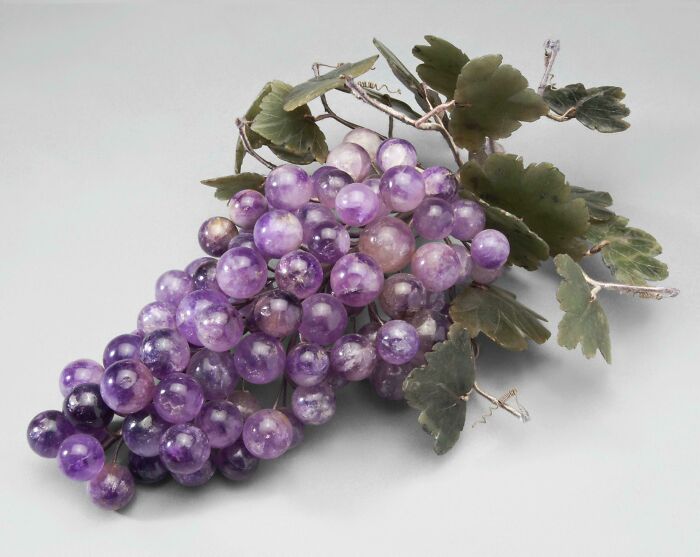 Ancient artefact of amethyst grapes with green leaves, showcasing historical craftsmanship.