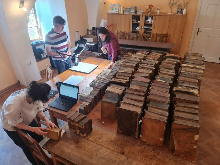 Researchers examine ancient artefacts and books on a wooden table in a study room.