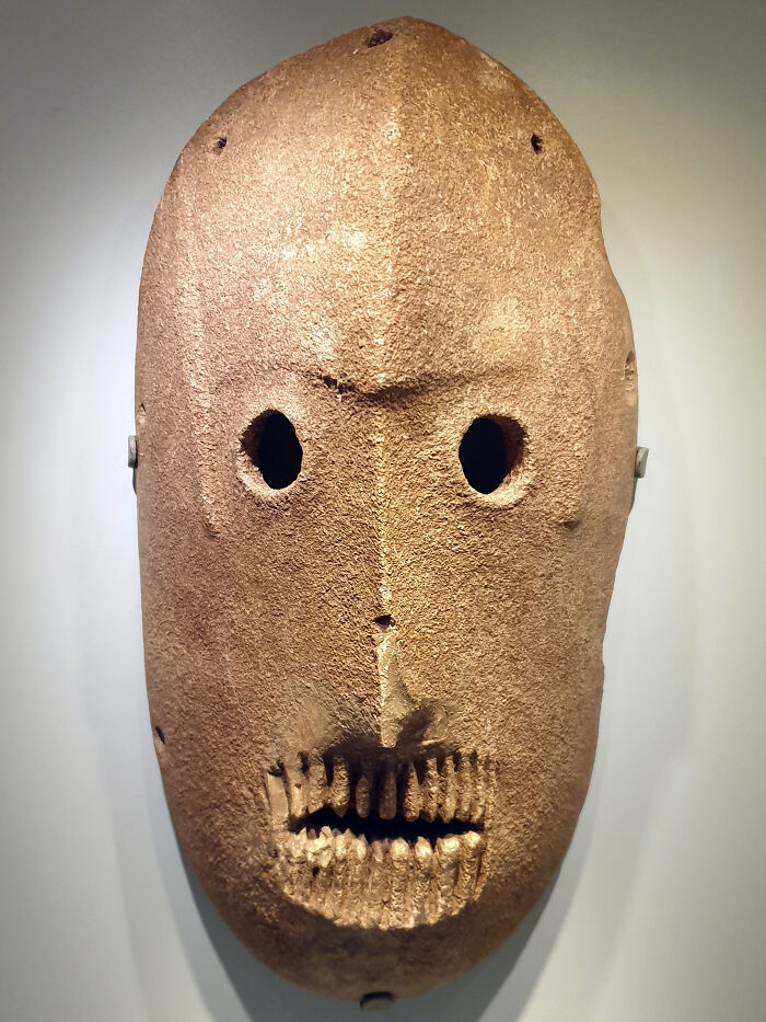 Ancient artefact mask with hollow eyes and carved teeth, showcasing survival through time.