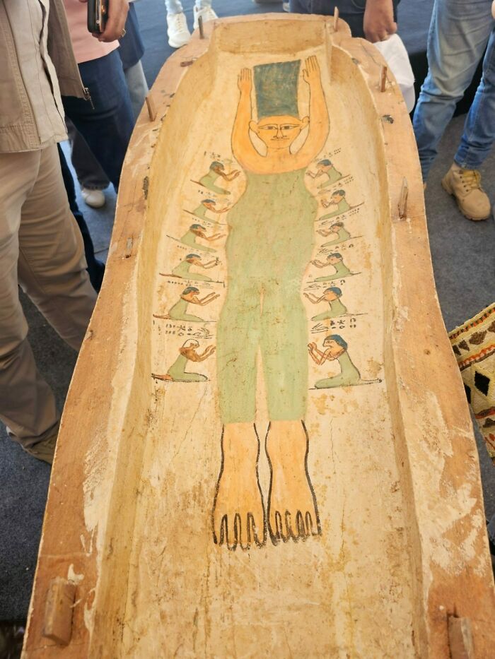 Ancient artefact with painted figures on a wooden surface, surrounded by people viewing the piece.