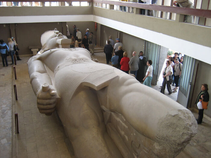 Ancient artefact: Large stone statue of a reclining pharaoh in a museum with visitors observing.