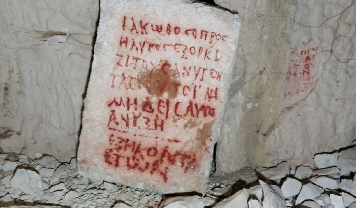 Ancient artefact with red inscriptions on stone, resting against a rocky wall.