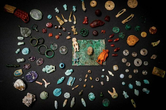 Ancient artefacts arranged on a dark surface, including various small sculptures, coins, and beads.