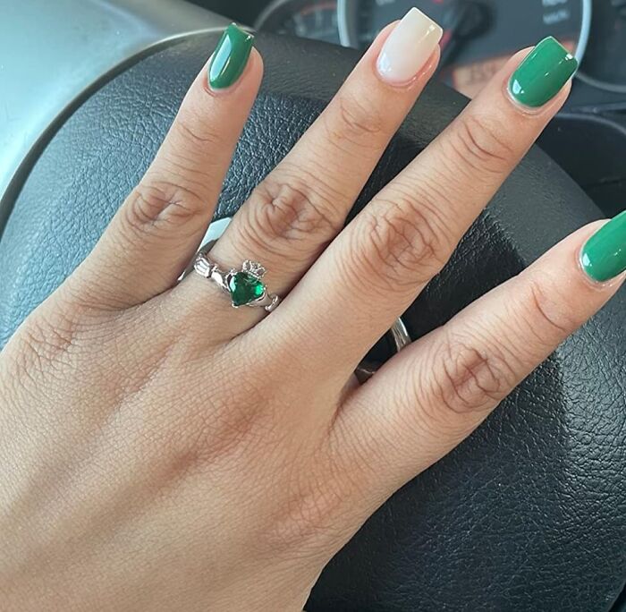 Hand with green nail polish and a ring on a vehicle steering wheel, highlighting a special gift.