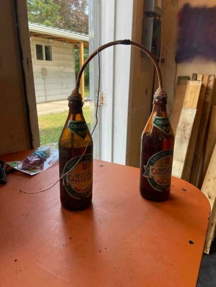 Two Okocim beer bottles connected by a wire, forming a mysterious object on an orange table.