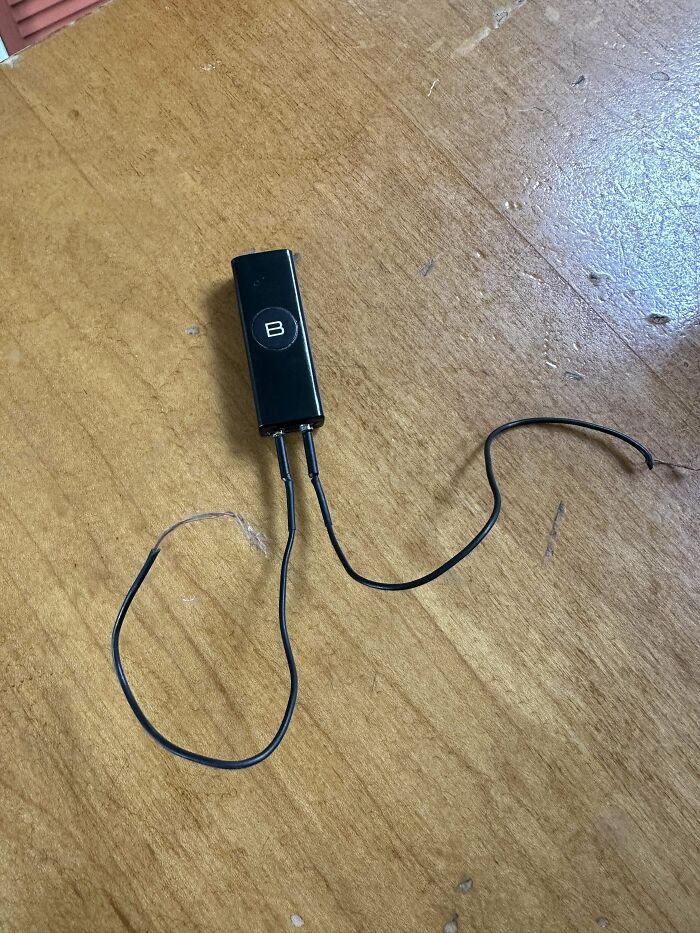 Weird object with a black rectangular body and two wires on a wooden surface.