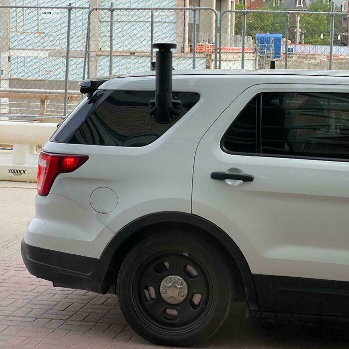 Unusual object on a white SUV, resembling a black cylindrical pipe near the rear window.
