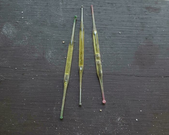 Weird objects: Three long glass sticks with colored ends on a wooden surface.