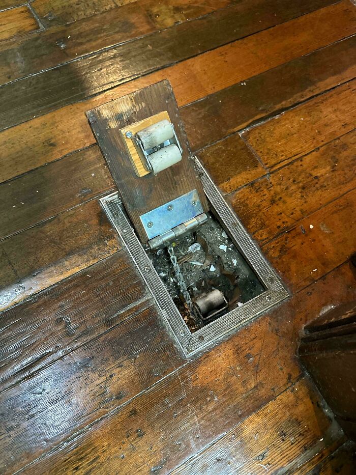 Weird objects: A wooden panel in a floor reveals a hidden mechanism with a chain and roller, surrounded by debris.