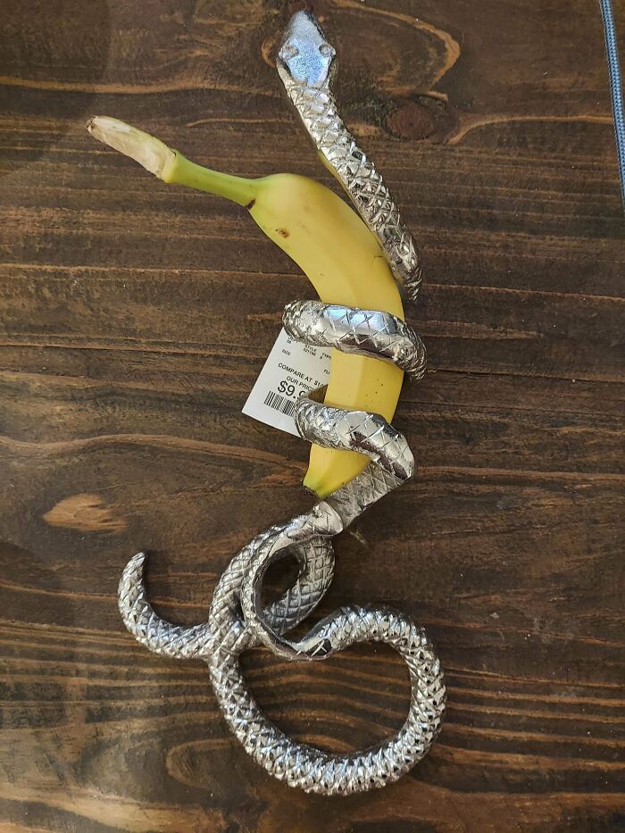 Weird object resembling a metal snake coiled around a banana on a wooden surface.