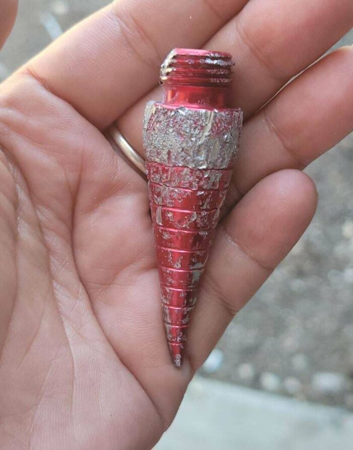 Hand holding a weird cone-shaped object with a threaded end, featuring red and silver colors.