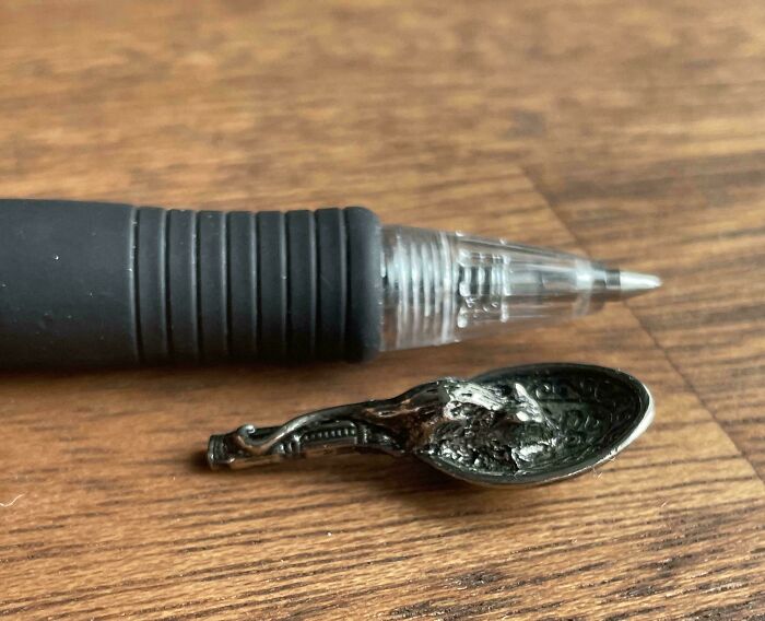 Weird object resembling an ornate spoon next to a pen on wooden surface.