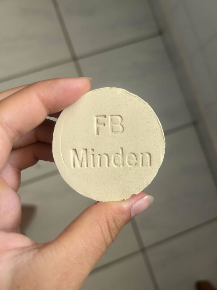 Hand holding a mysterious round object labeled "FB Minden," a strange item found by someone.
