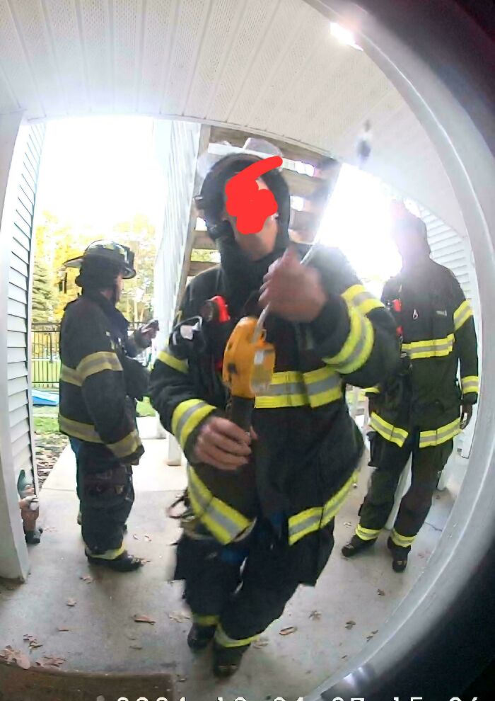 Firefighters in gear holding equipment on a porch, captured from a doorbell camera.