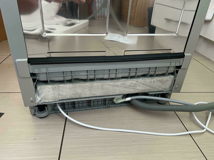 Unusual object beneath kitchen appliance, including hoses and cables, on tiled floor.