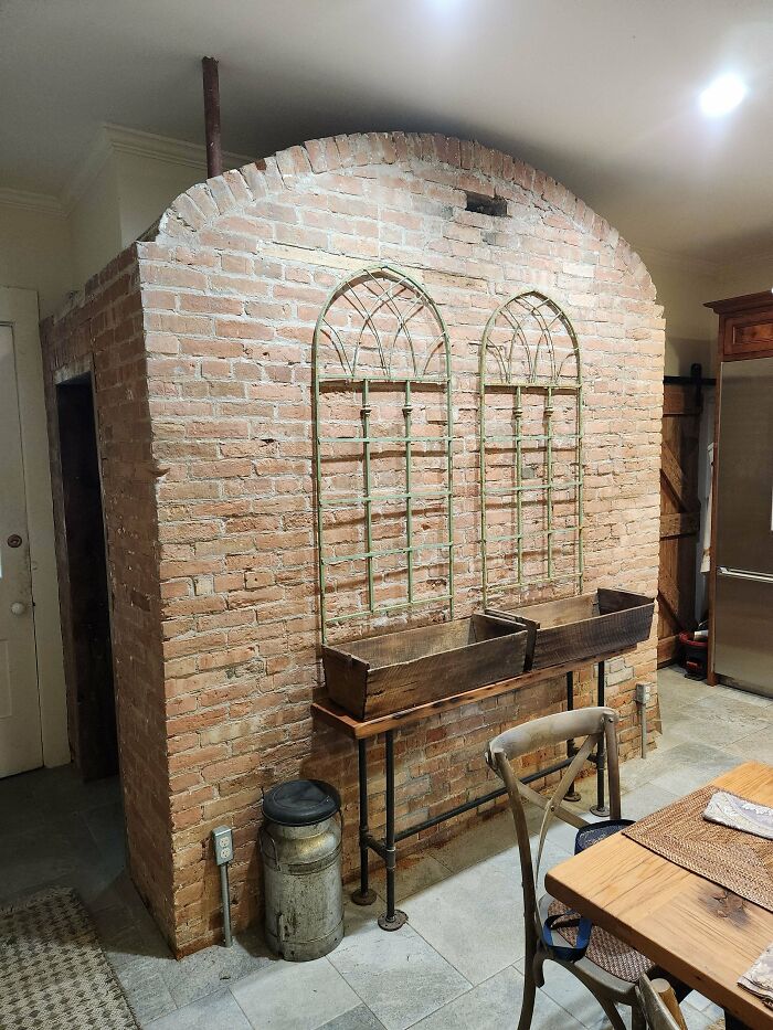 Brick structure indoors with arched metal decorations and wooden planters, resembling a vintage oven or storage space.