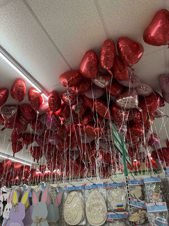 Red heart-shaped balloons in a store ceiling overflowing with seasonal decorations, highlighting consumerism excess.