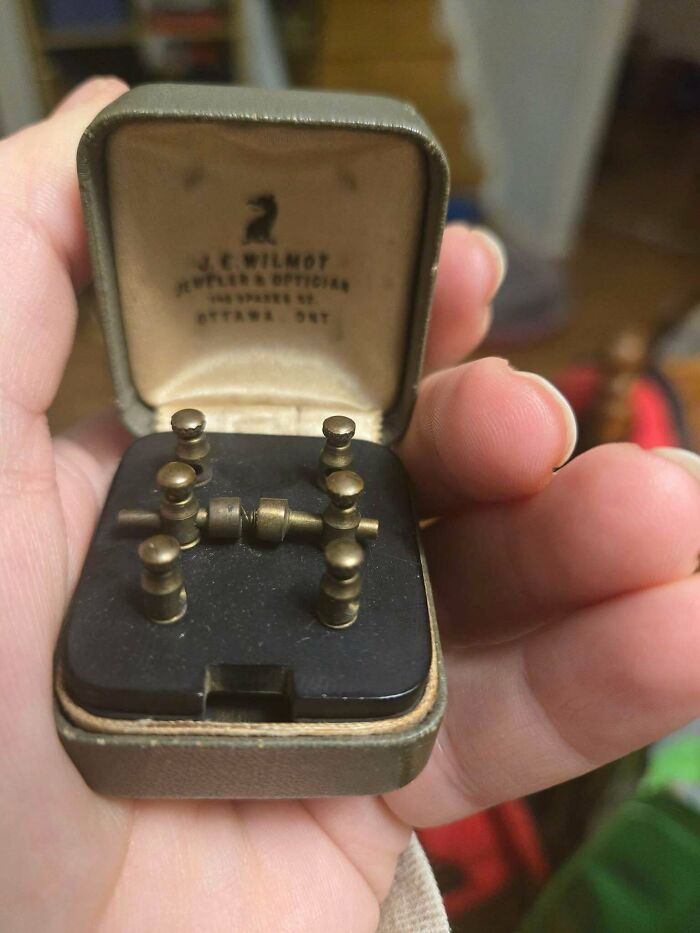 A person holds an antique J.E. Wilmot jewelry and optics box containing a mysterious object with small brass components.