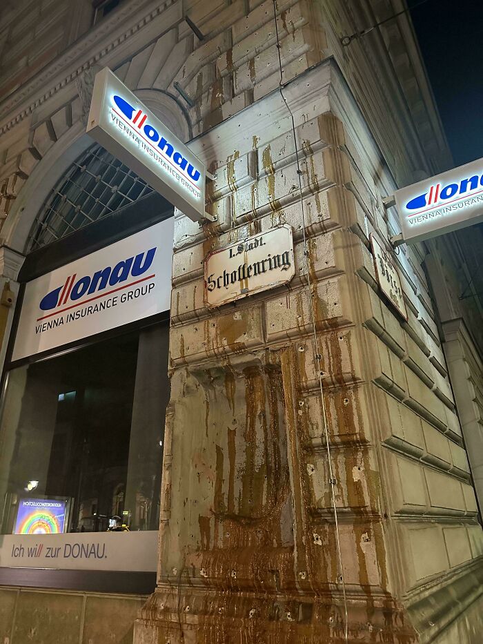 Old building corner with stained wall and "Donau Vienna Insurance Group" sign, encountering a weird object on Schoenbrung Street.