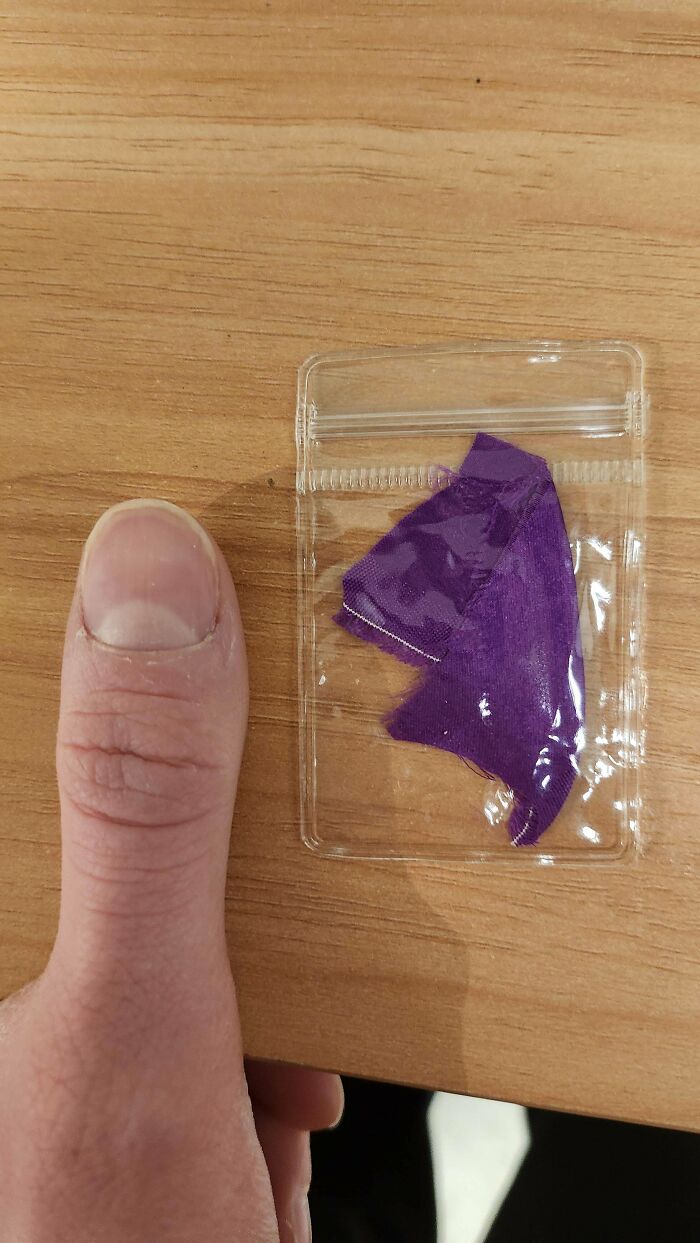 Weird object: tiny purple fabric piece in a small plastic bag next to a thumb for scale.