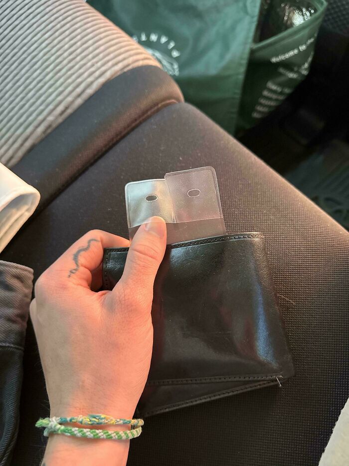 Hand holding a black wallet with transparent, weird objects inside.