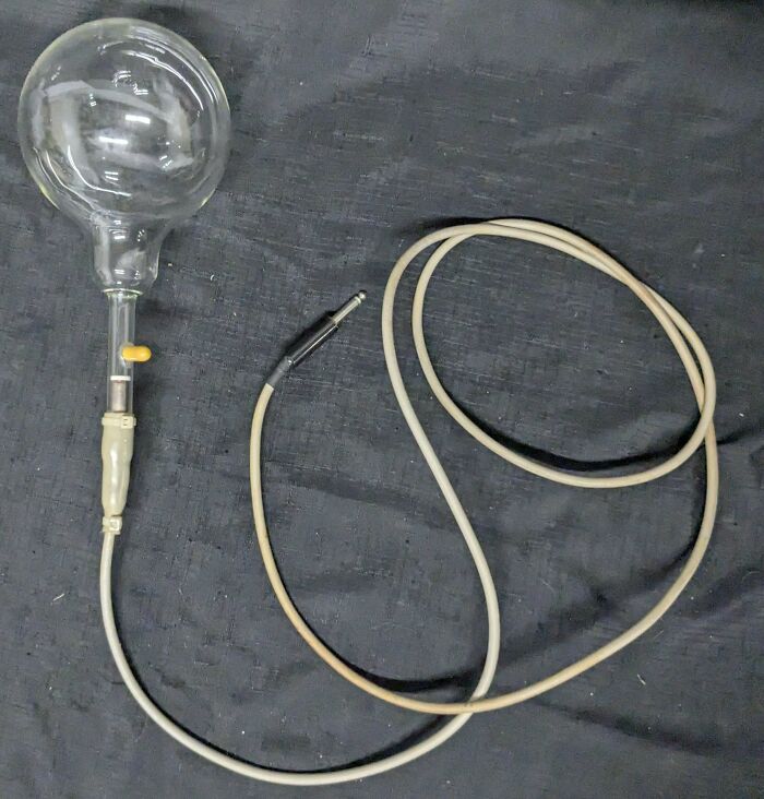 Weird object: a glass bulb connected to a cord with a plug, lying on a dark surface.