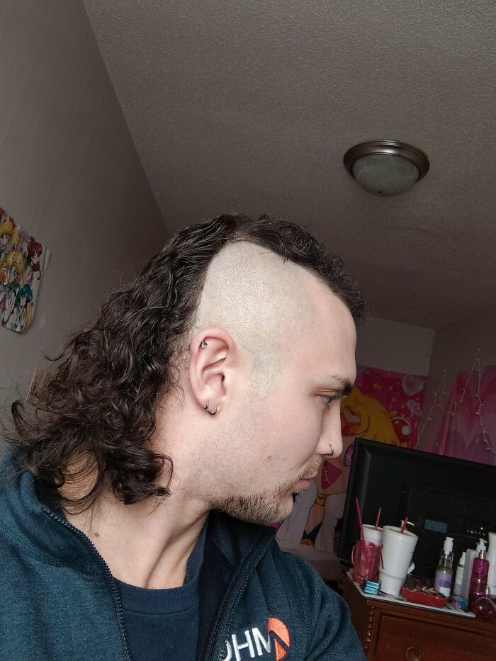 Man with an unfortunate haircut, sporting a half-shaved head and long curly hair on the other side.