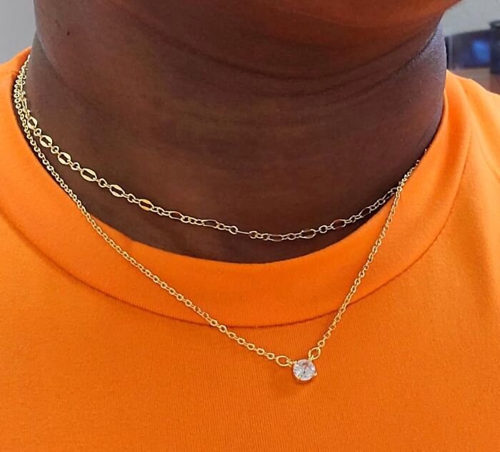Gold necklace gift from Reddit, worn over an orange shirt, featuring a simple design with a sparkling pendant.