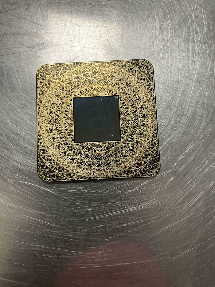 Unusual ornate square object with intricate gold patterns on a metallic surface.