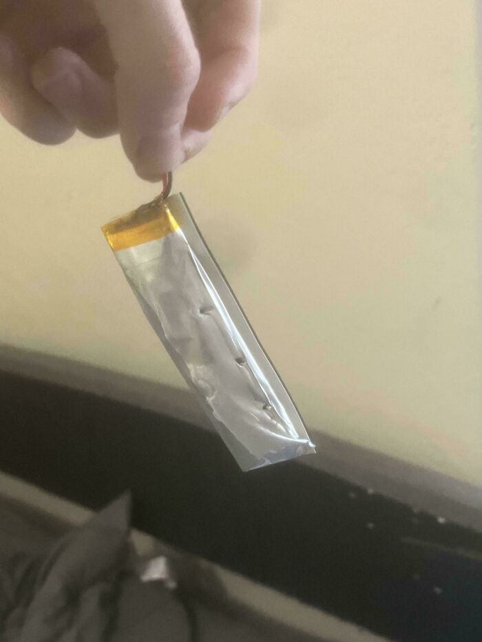 Hand holding a weird object with a metallic casing and wires, resembling a small battery or electronic component.