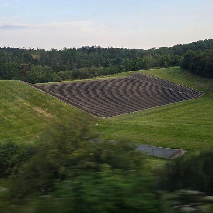 Mysterious stepped structure in a grassy landscape surrounded by trees.