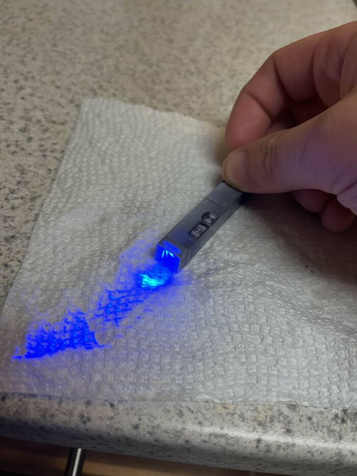 Hand holding a small device emitting blue light onto a napkin, related to weird objects.