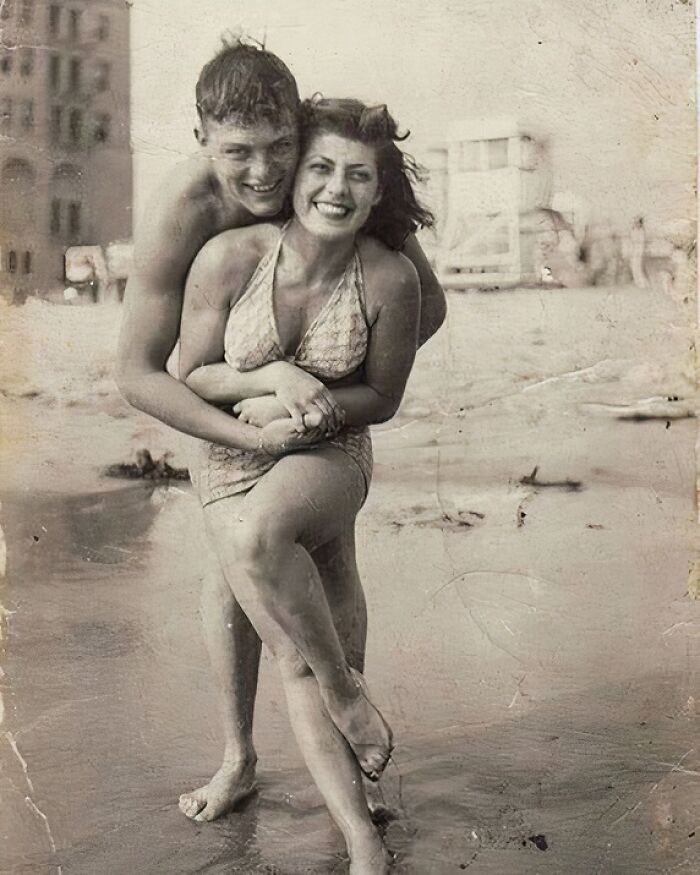 A couple laughing and embracing on a beach, capturing true happiness in a vintage photograph.