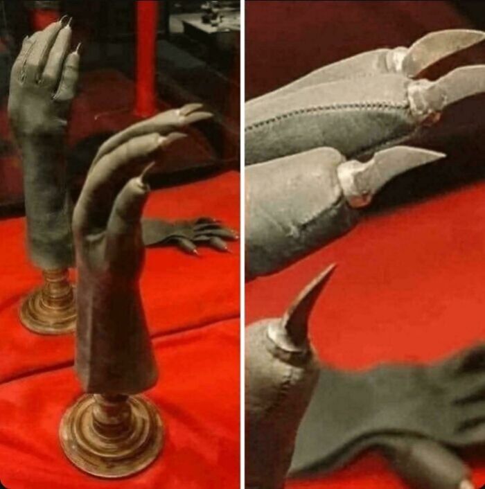 Ancient artefacts: two clawed gloves displayed on stands against a red background.