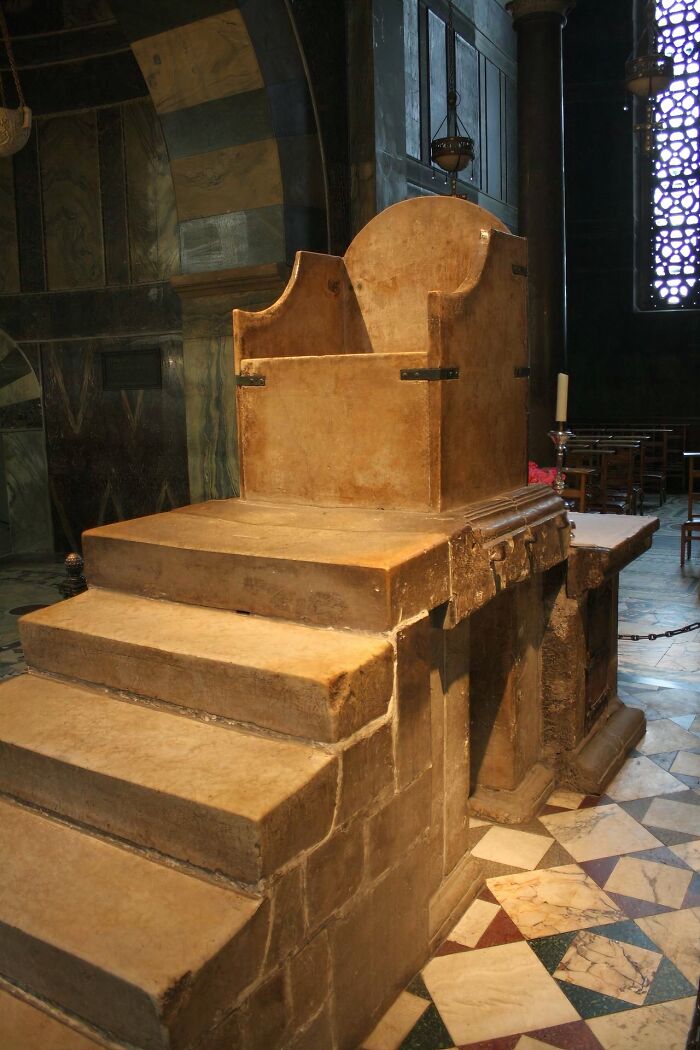 Ancient artefact: A historic stone throne with steps, preserved in a dimly lit room with patterned floor tiles.