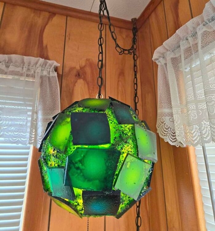 DIY craft project with a green, geometric light fixture hanging against a wood-paneled wall.