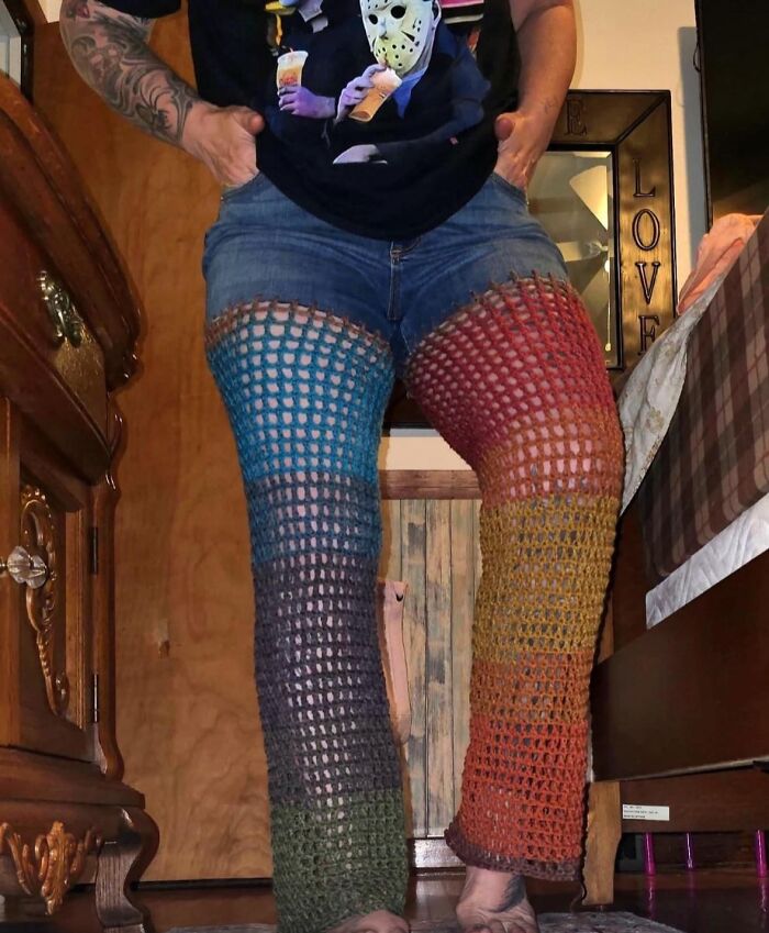 Man wearing jeans altered with colorful, crochet leg panels in a comically odd DIY craft project.