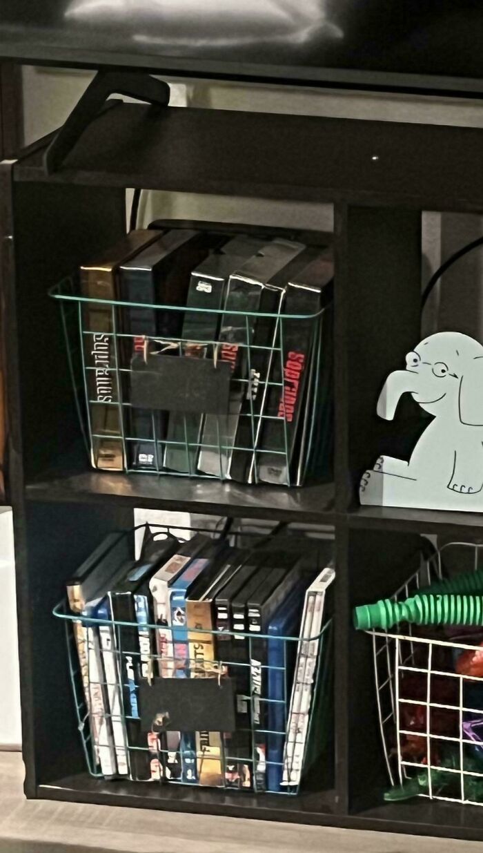 Shelf with VHS tapes and DVDs organized in baskets, possibly a collection by annoying boyfriends or husbands.