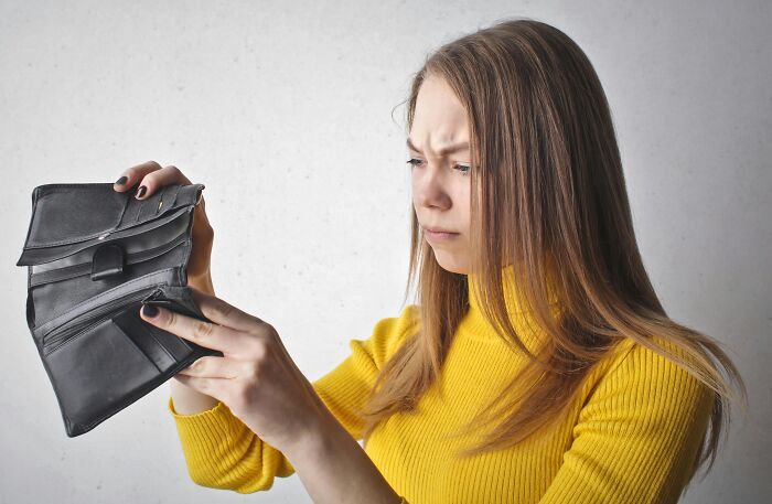Woman in a yellow sweater looking at an empty wallet, symbolizing work-struggles.