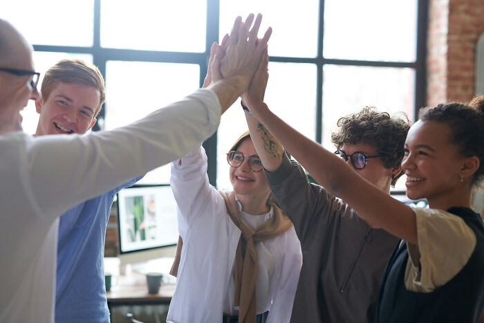 A diverse group of coworkers high-fiving, symbolizing overcoming work-struggles in a collaborative office environment.