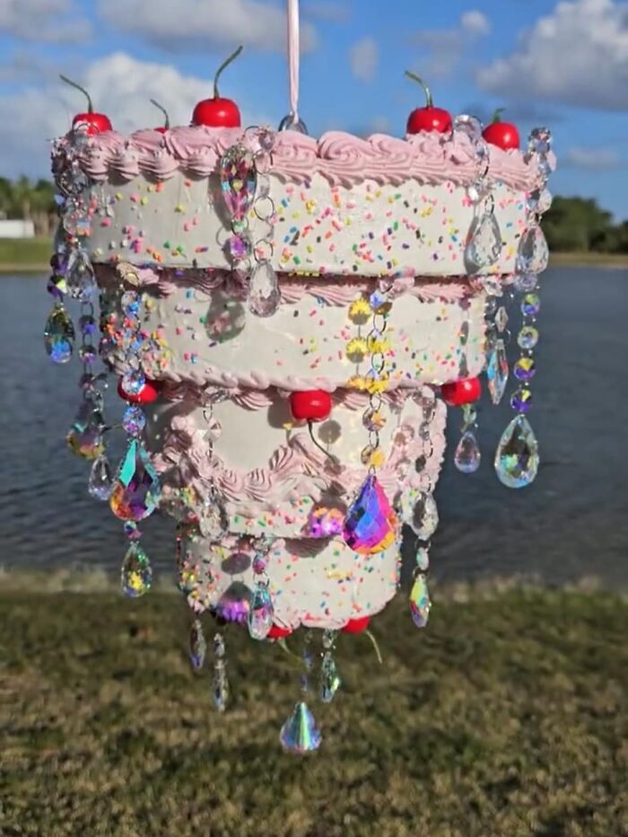 Upside-down cake-shaped DIY chandelier with faux cherries and crystals hanging outdoors, showcasing craft shaming creativity.