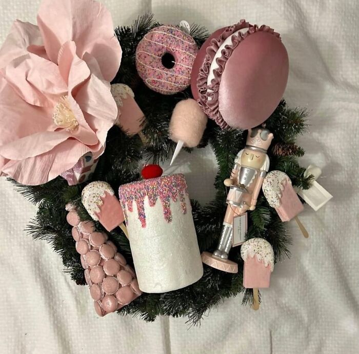 Wreath with pink DIY crafts including a nutcracker, macarons, cake, and flowers, exemplifying horrendous craft projects.