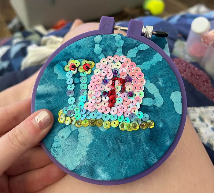 Sequined snail design with vivid colors, crafted on blue fabric in a hoop, showcasing a creative DIY project.