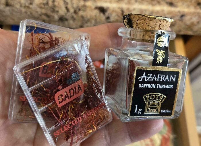 Hand holding small containers of saffron threads, showcasing dumpster diving treasures raccoons would be wowed by.