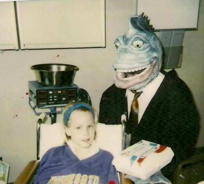 Young girl in Minnesota sweatshirt sitting next to a person in a dinosaur costume in an awkward family photo.