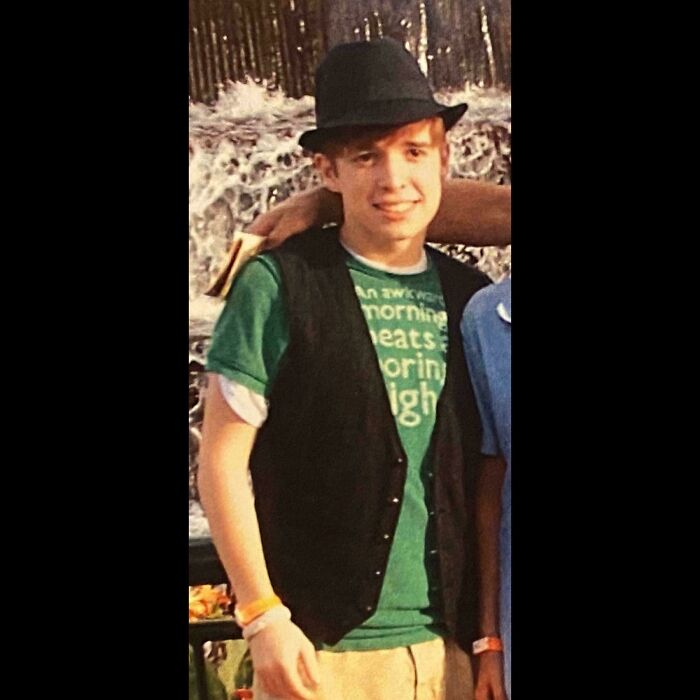 Young man wearing a green t-shirt, black vest, and fedora, captured in a memorable cringe-worthy regrettable past photo.