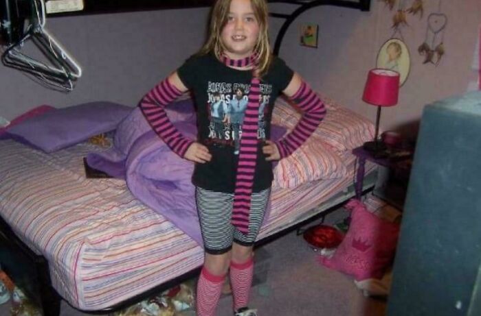 Child in a colorful striped outfit posing in a bedroom, one of many regrettable past pics causing cringe today.
